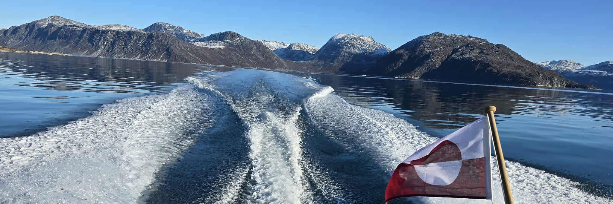 Skumsprøjt agter på båd, der sejler langs de grønlandsk bjerge