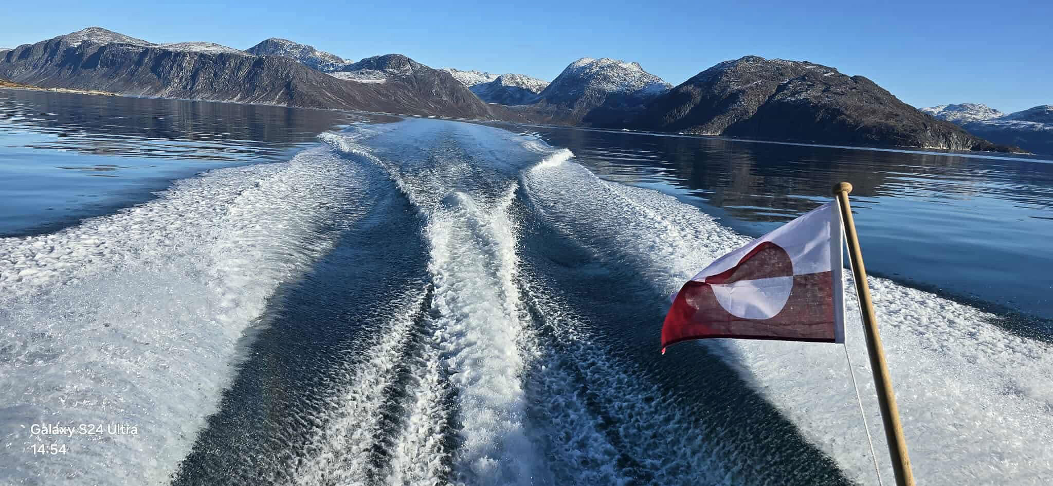 Skumsprøjt agter på båd, der sejler langs de grønlandsk bjerge